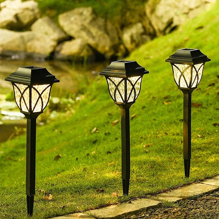 Three solar garden lights on a grassy area with a stone path and water in the background.