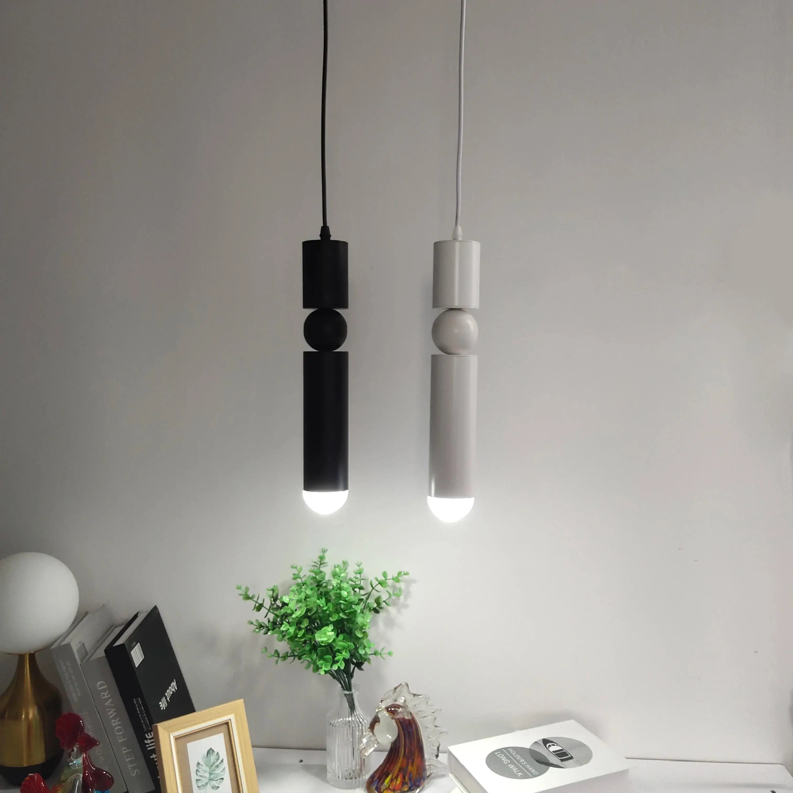 Two modern pendant lights hanging against a plain wall with decorative items on a surface below.