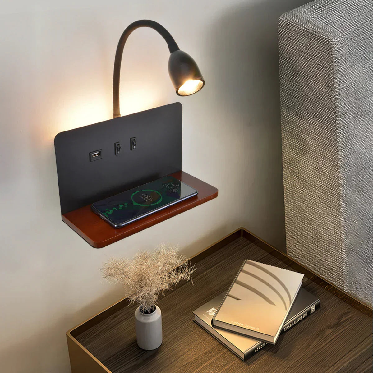 Wall-mounted charging station with USB ports and a smartphone on a wooden shelf, next to a book and small plant.