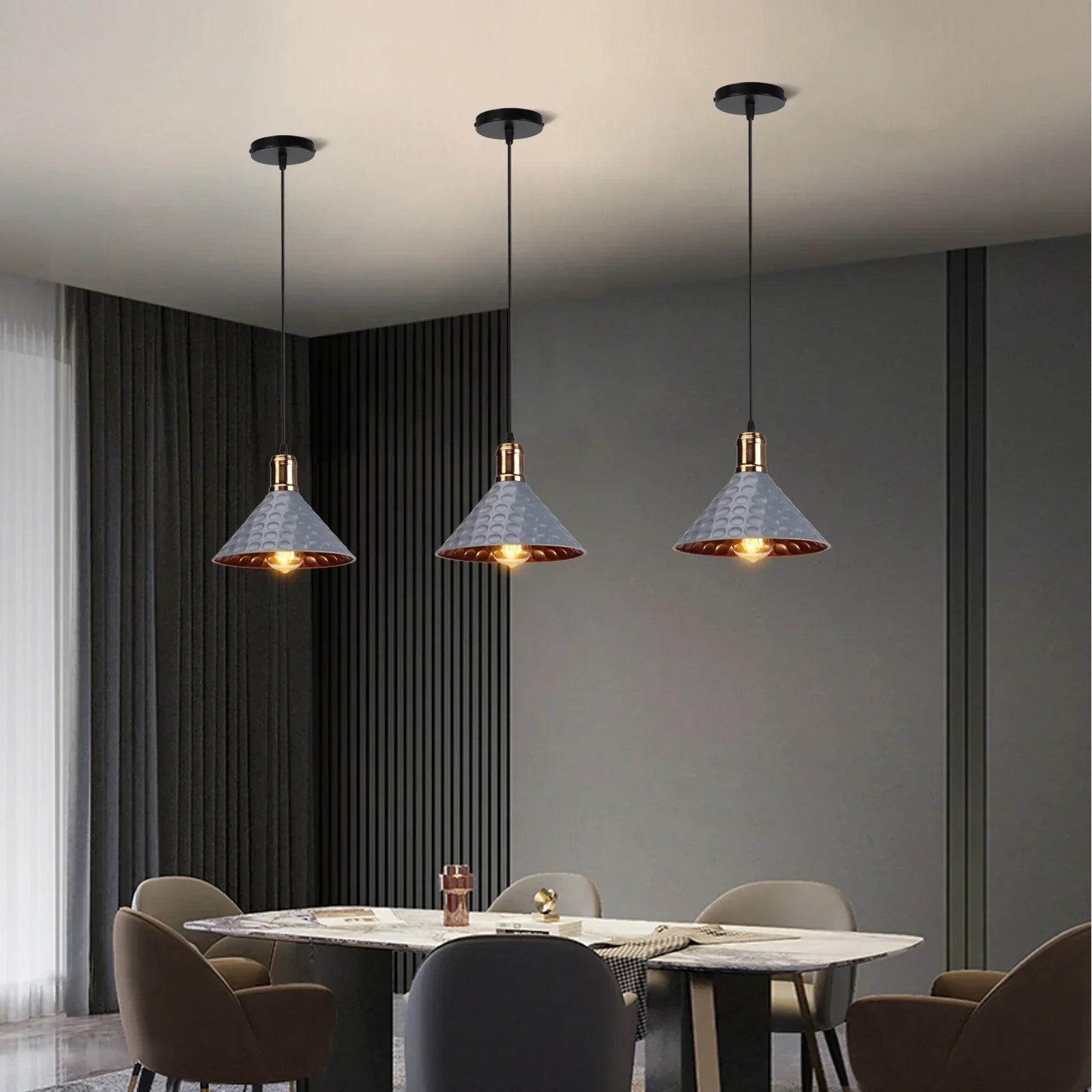 Set of three gray and gold pendant lights hanging above a modern dining table in a dark-toned room.