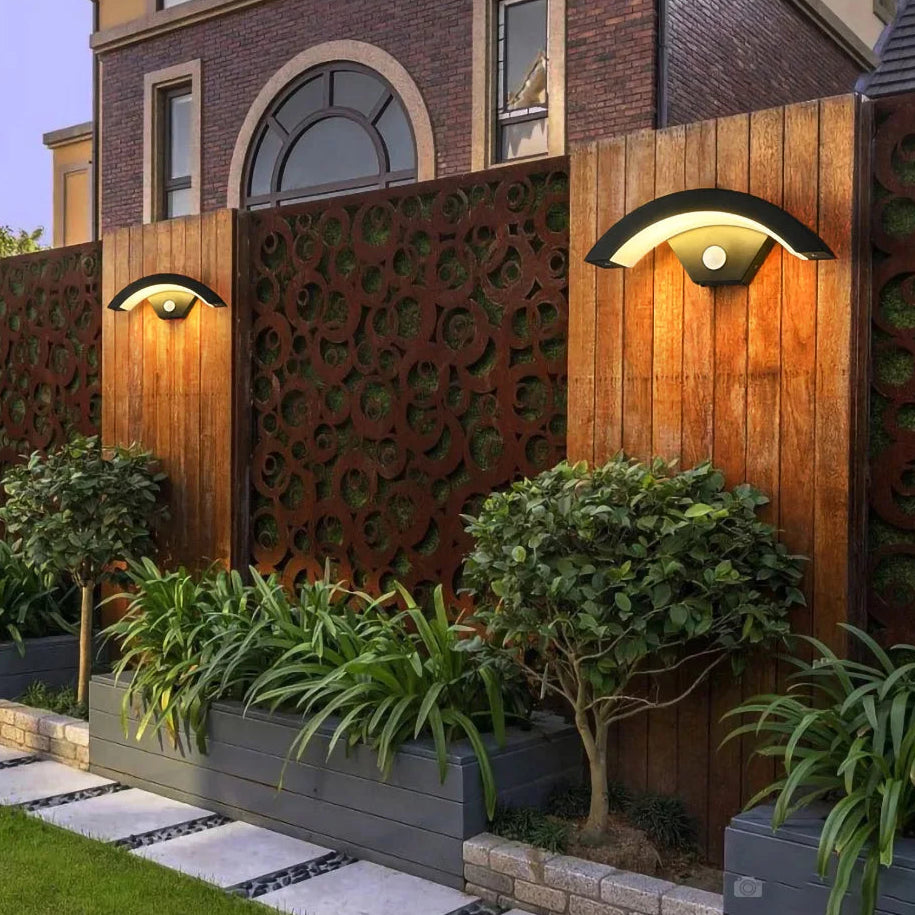 Decorative outdoor wall light fixture with plants and a building in the background