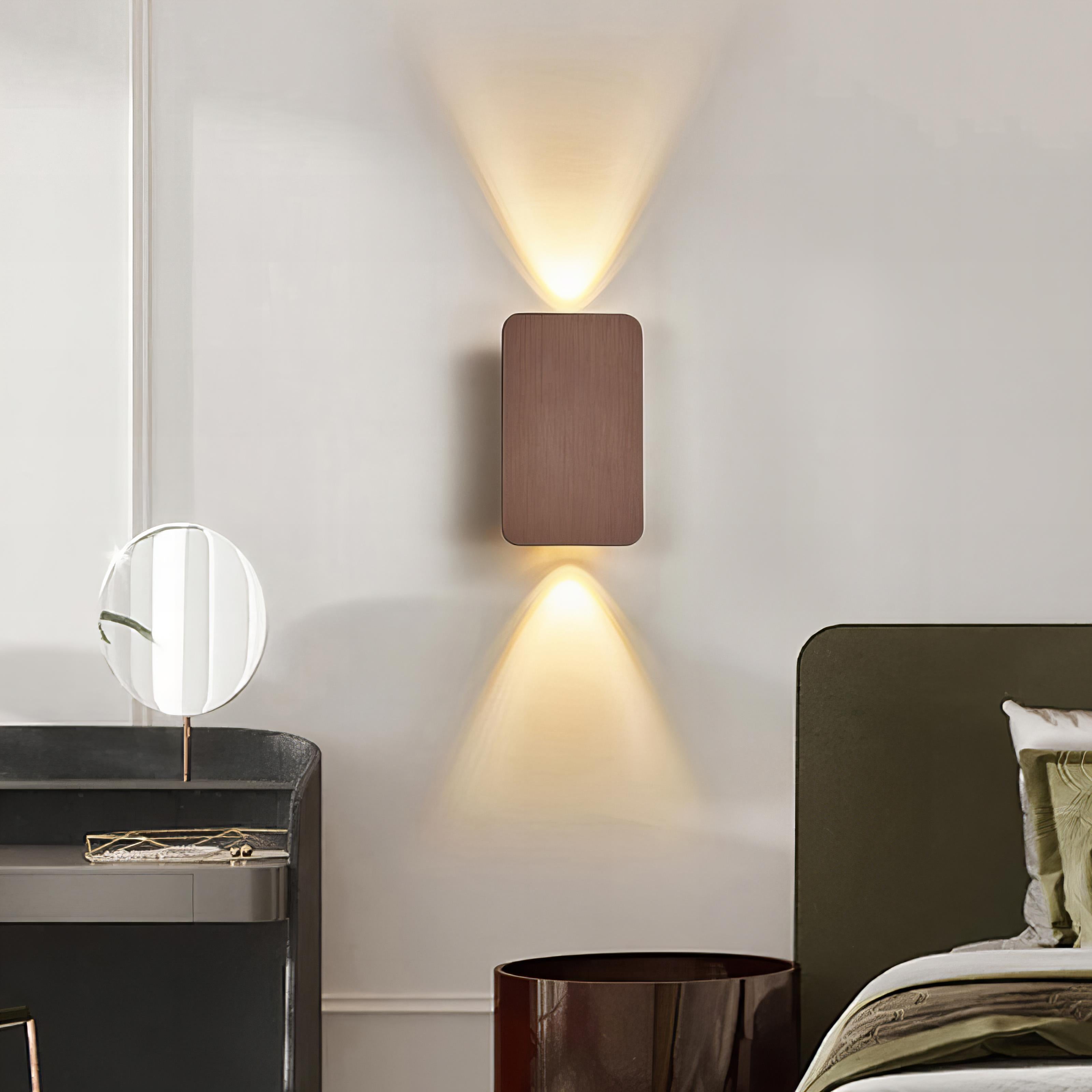 Modern wall lamp on a neutral wall with a bed and nightstand in the foreground