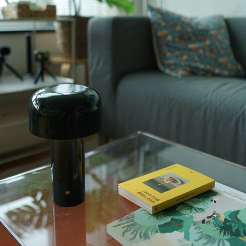 Black object on a glass coffee table with books in a living room setting