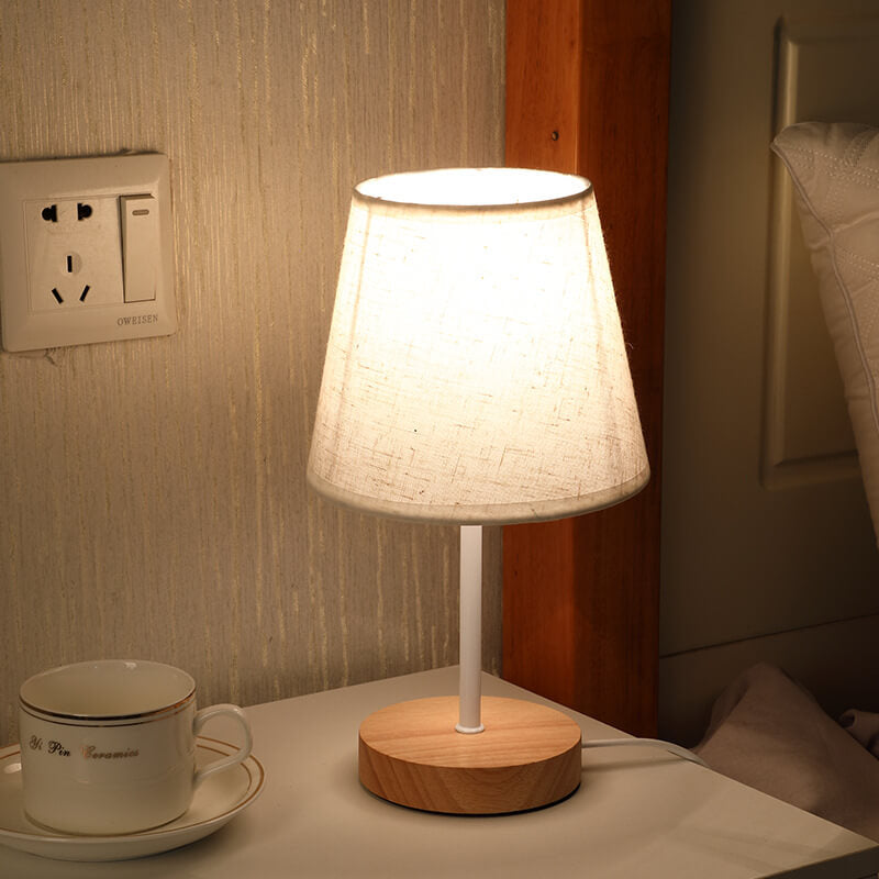 Table lamp with wooden base on a nightstand next to a cup and saucer.