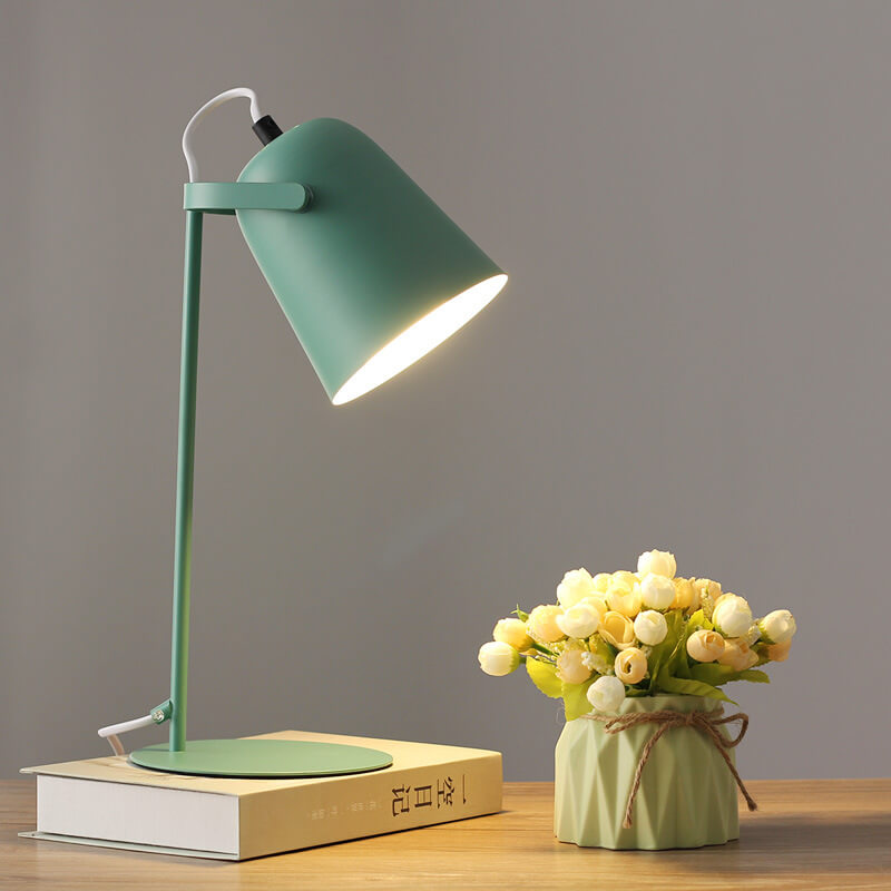 Green desk lamp on a wooden surface with a small vase of flowers next to it.