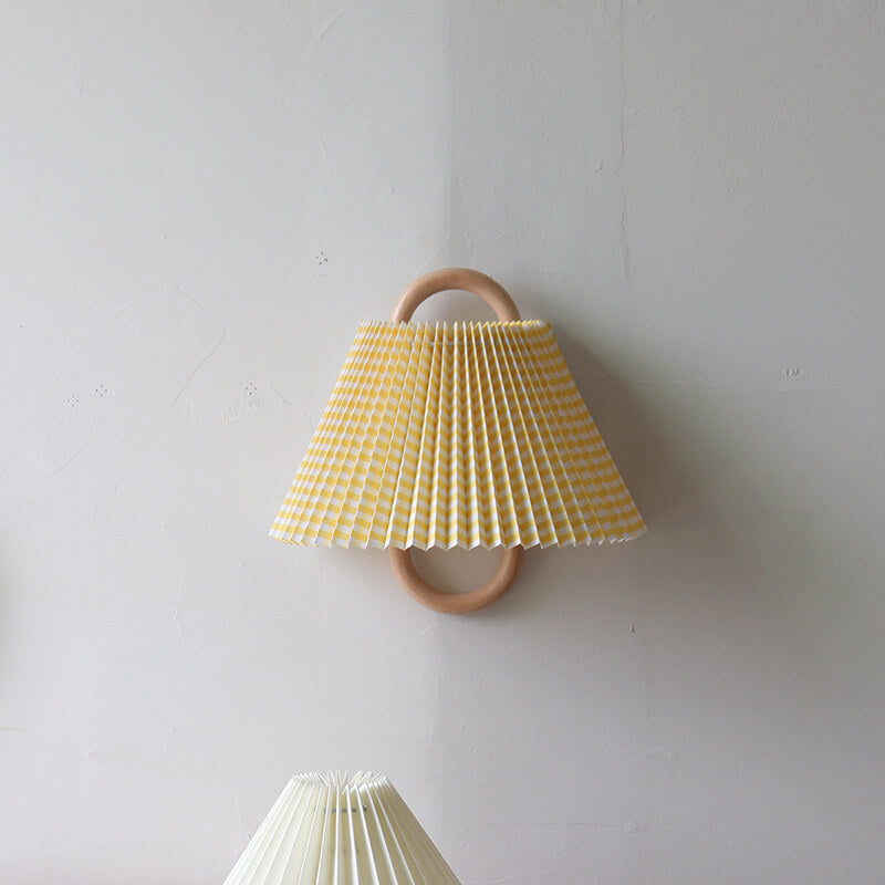 Yellow pleated lampshade with wooden ring on a white wall