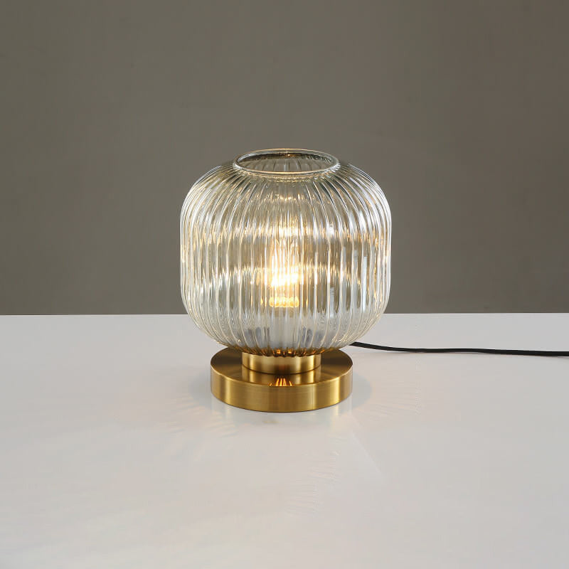 Table lamp with ribbed glass shade and gold base on a white surface with gray background