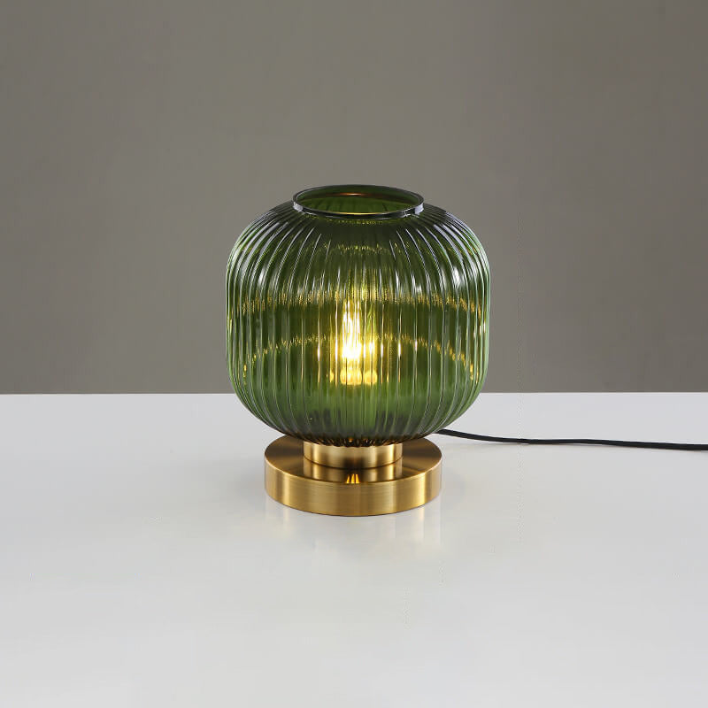 Green ribbed glass table lamp with gold base on a white surface and gray background