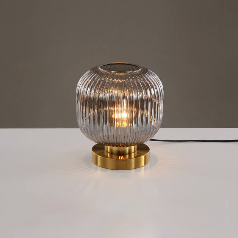 Table lamp with ribbed glass shade and gold base on a white surface with a gray background