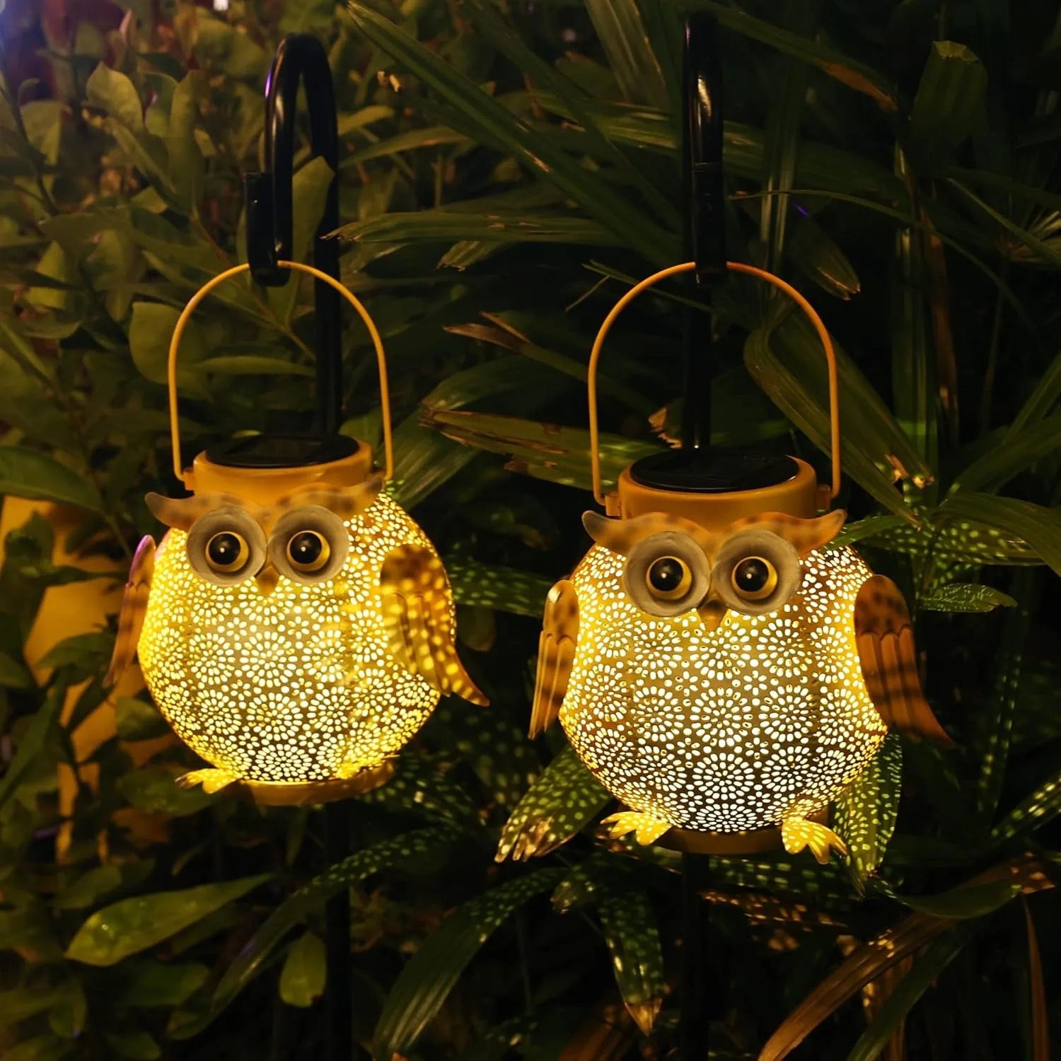 Two owl-shaped solar lights hanging among green plants at night.