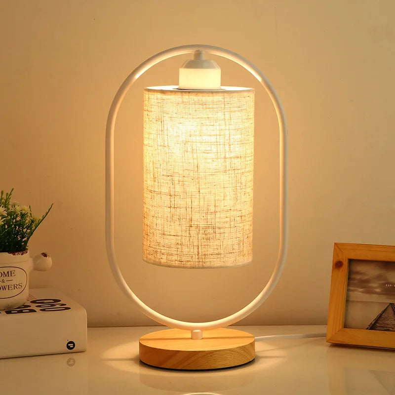 Table lamp with wooden base and fabric shade on a table, emitting warm light.