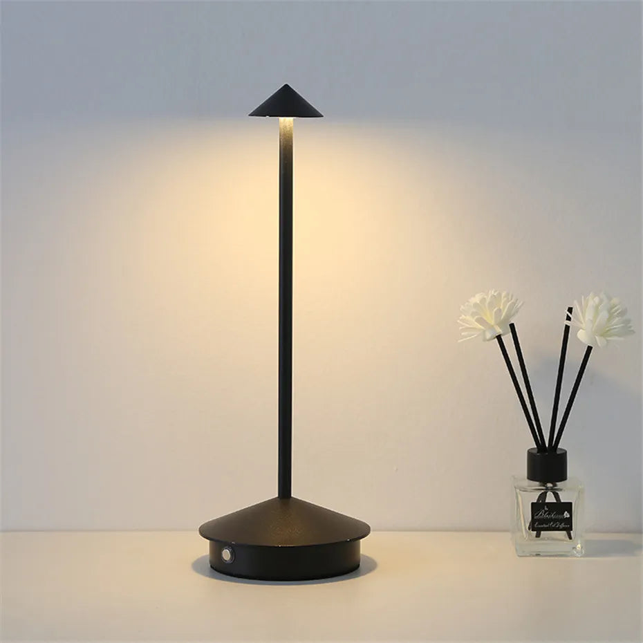 Black table lamp on a white surface with a diffuser bottle in the background