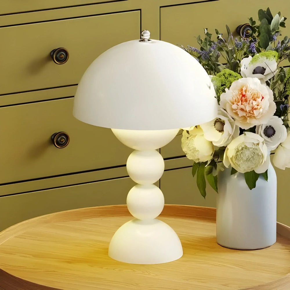 White table lamp on a wooden surface with a vase of flowers in the background.
