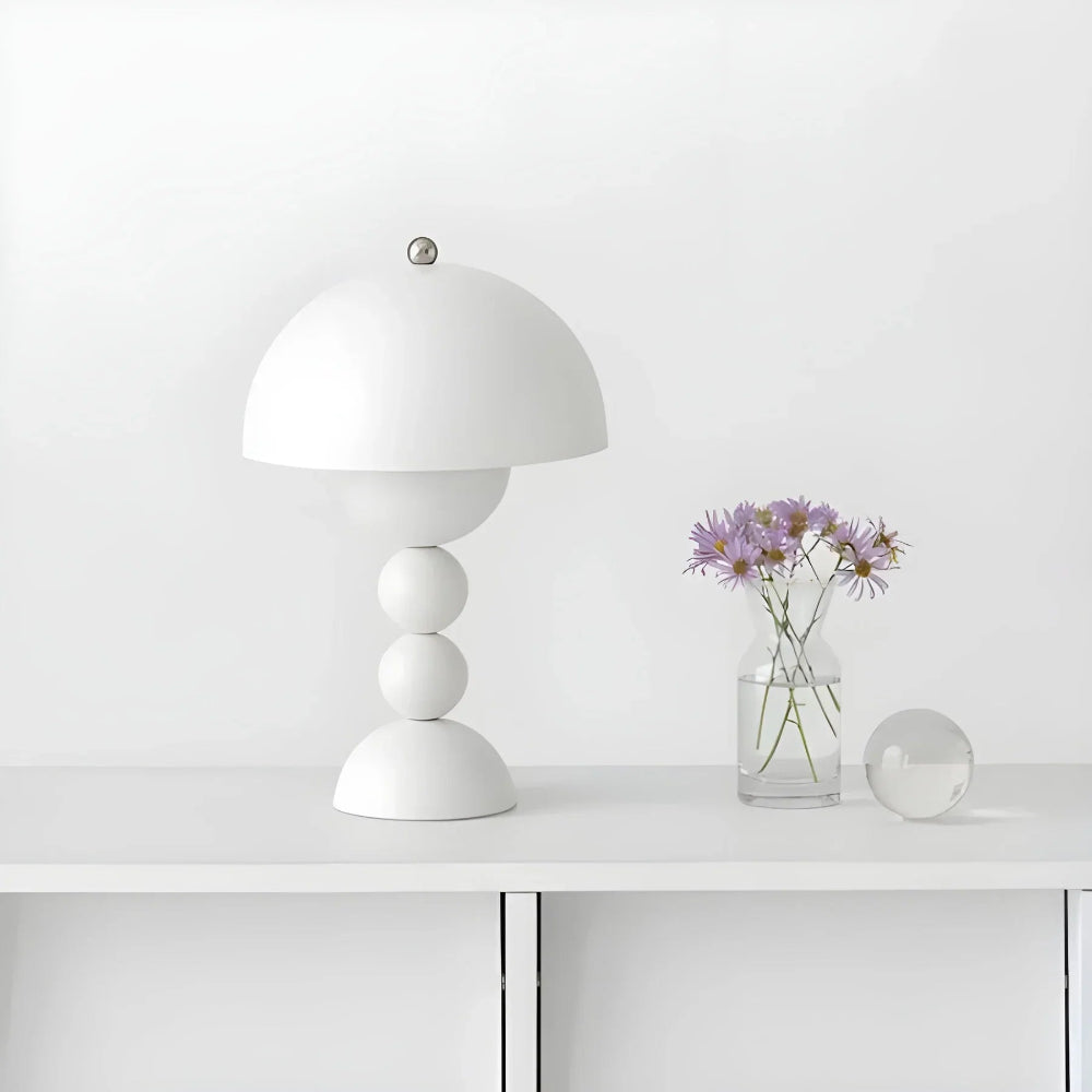 White table lamp on a white surface with a vase of flowers and a small round object.