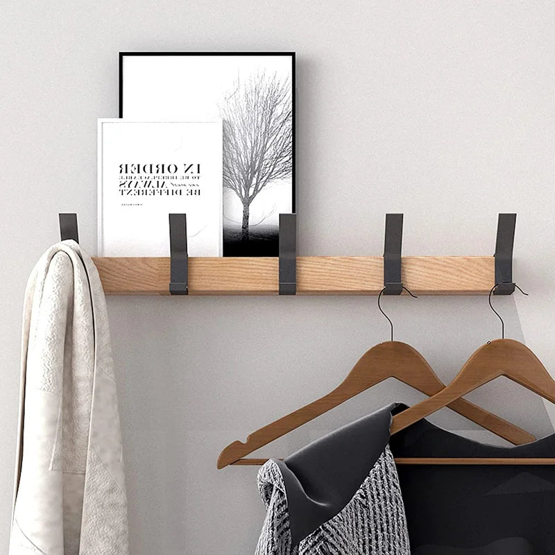 Wooden coat rack with hooks, framed artwork, and hangers against a white wall.