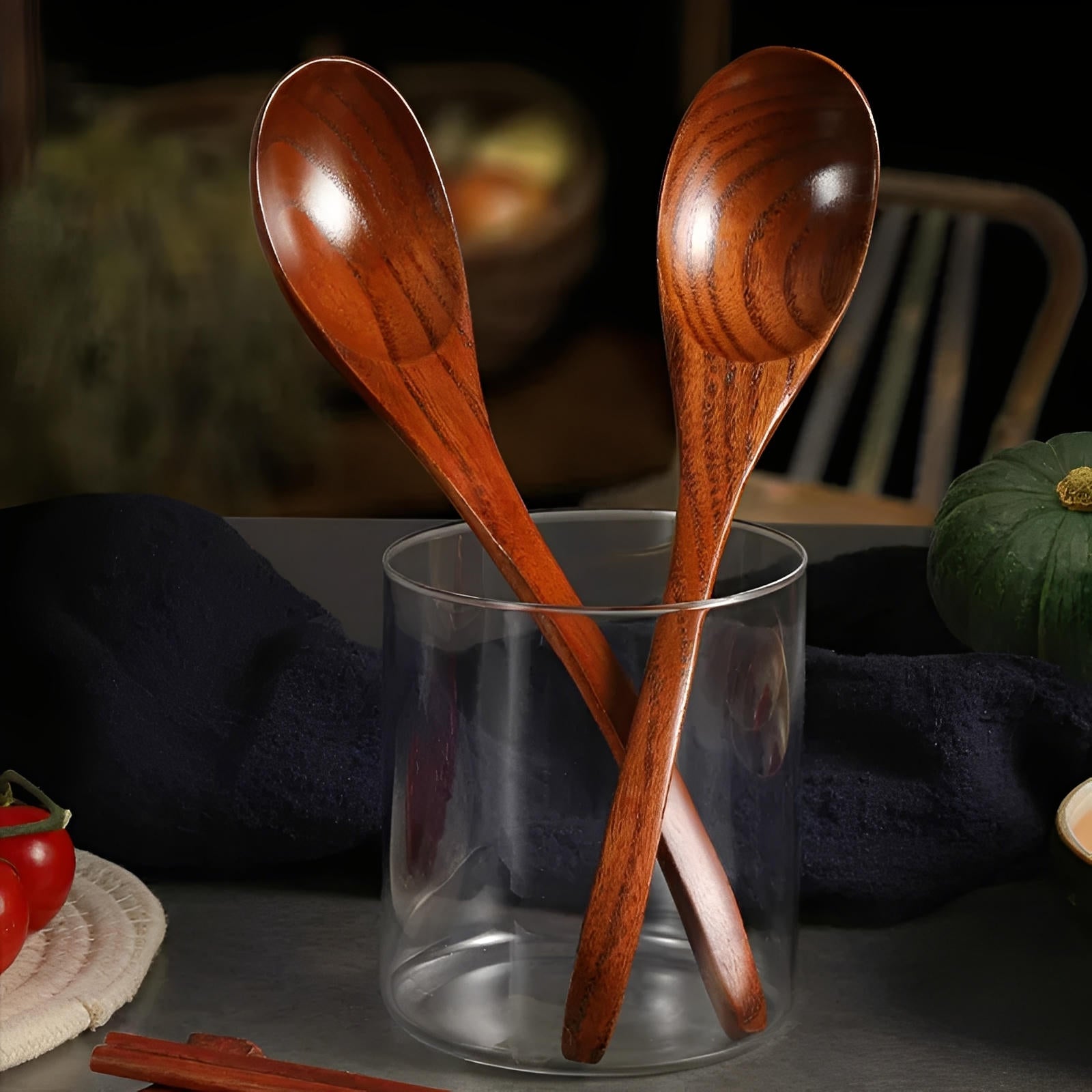 Two wooden spoons in a clear glass on a dark surface with a blurred background.