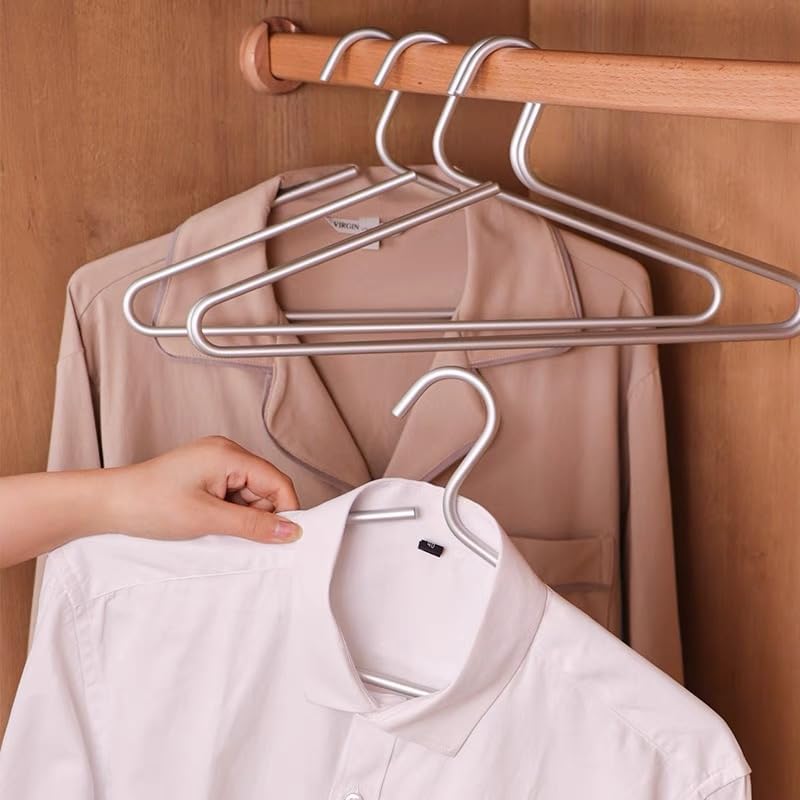 Person hanging a white shirt on a metal hanger with a beige jacket in the background.