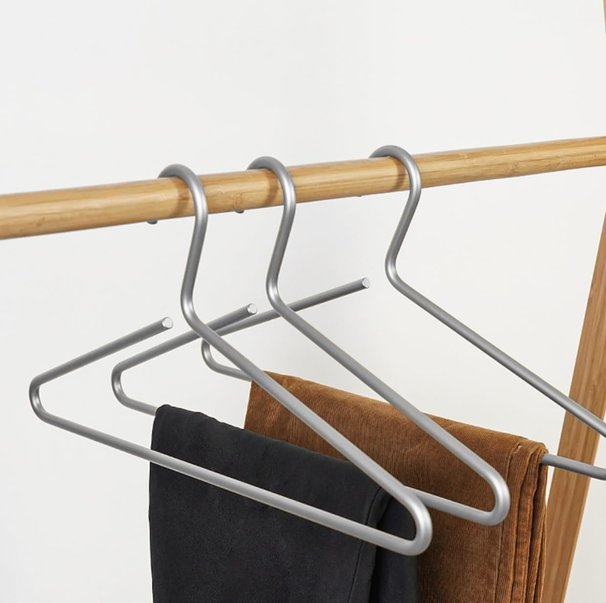 Metal hangers with clothes on a wooden rod against a white background