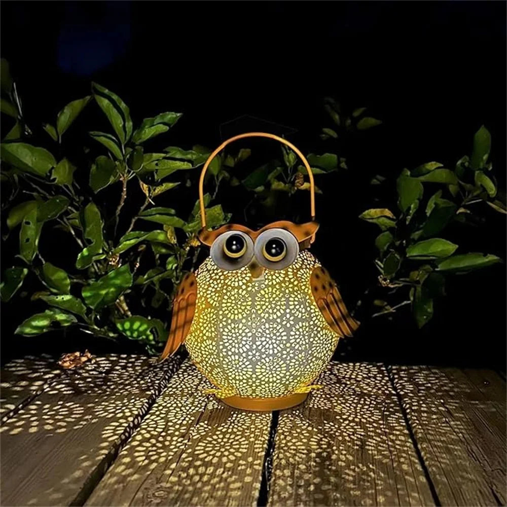 Owl-shaped lantern with a glowing light, placed on a wooden surface with greenery in the background.