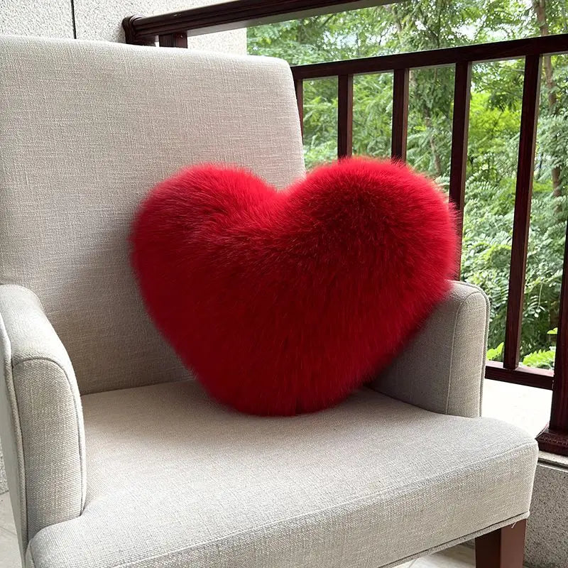 Red heart-shaped pillow on a gray chair with a blurred green outdoor background