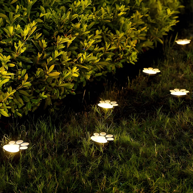 Solar-powered garden lights shaped like paw prints on grass and near bushes.
