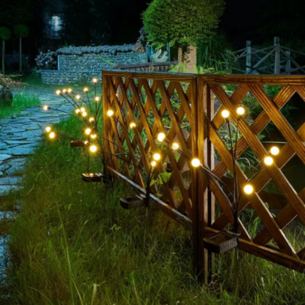 String lights on a wooden lattice fence in a garden setting at night.