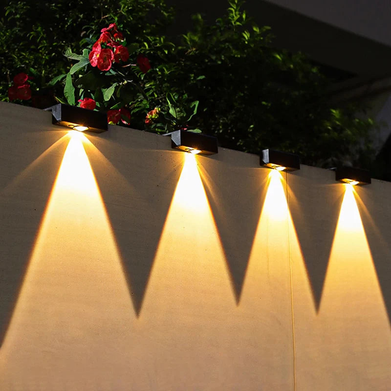 Solar-powered outdoor lights on a wall with plants in the background