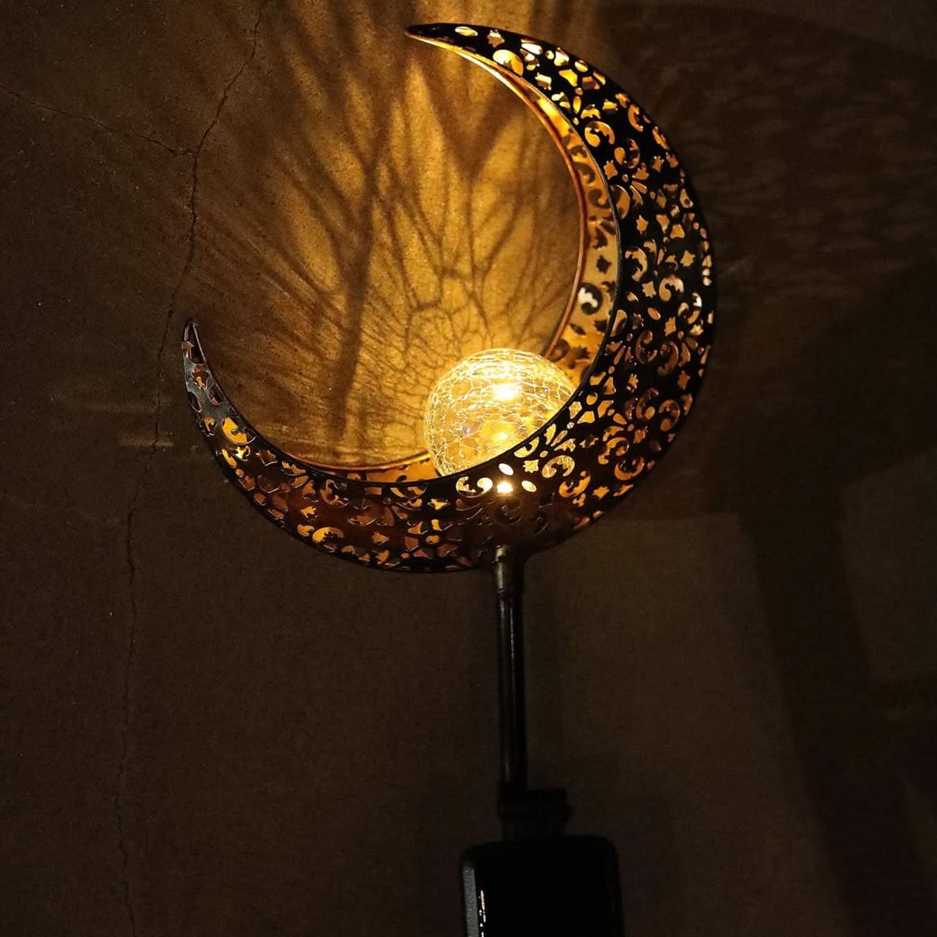 Decorative wall light shaped like a crescent moon with intricate patterns on a dark background.