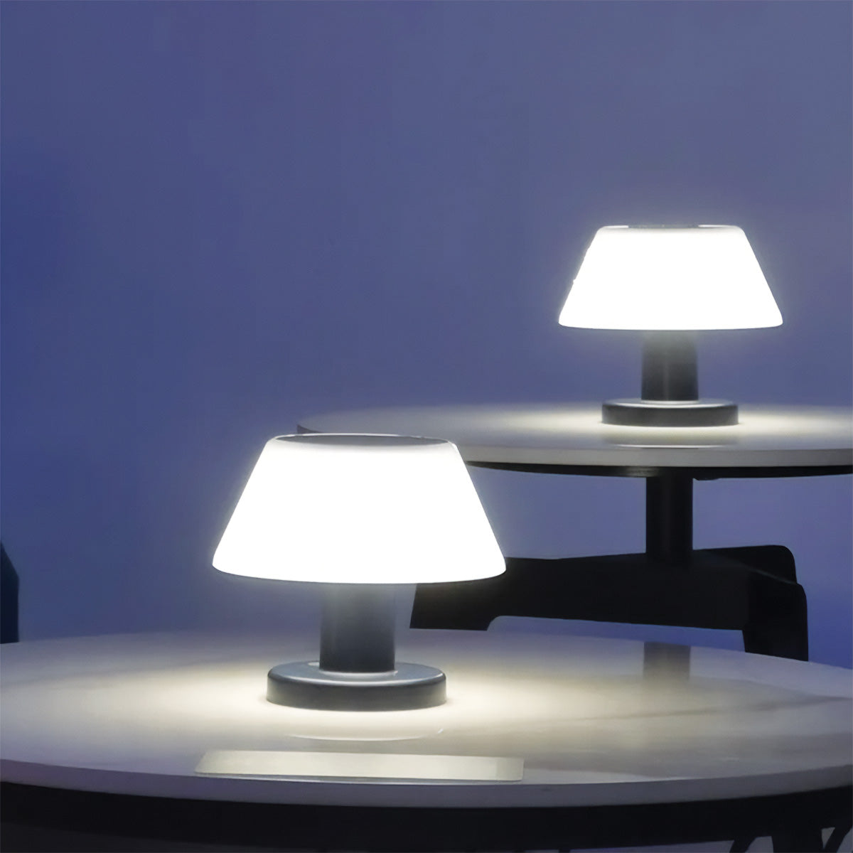 Two table lamps on round tables with a dark blue background