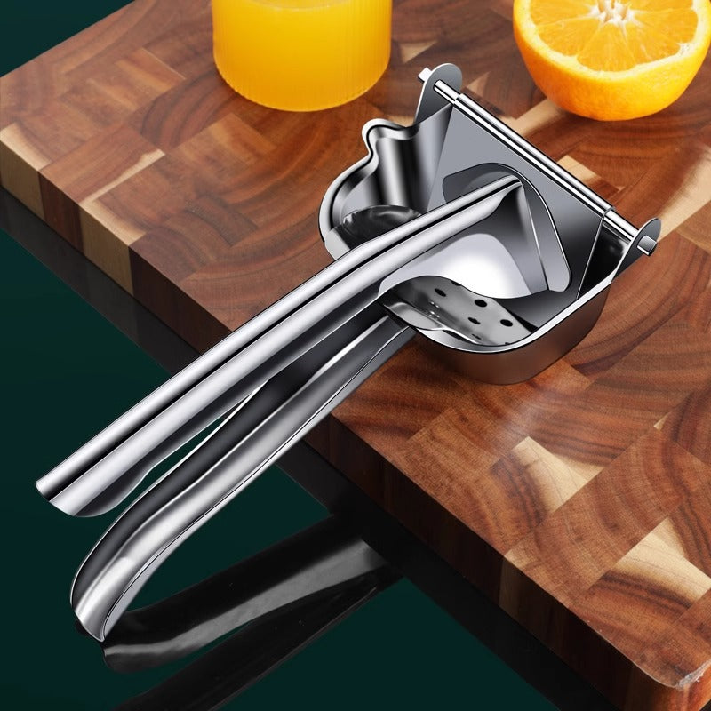 Stainless steel manual juicer on a wooden cutting board with an orange and a glass of juice.