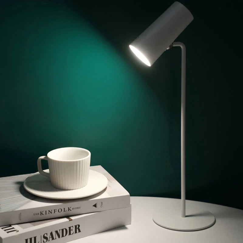 White desk lamp illuminating a white cup and books on a dark green background