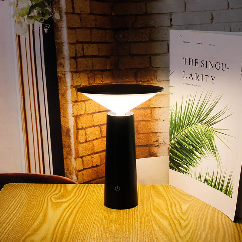 Black lamp on a wooden table with a book titled 'The Singularity' in the background.