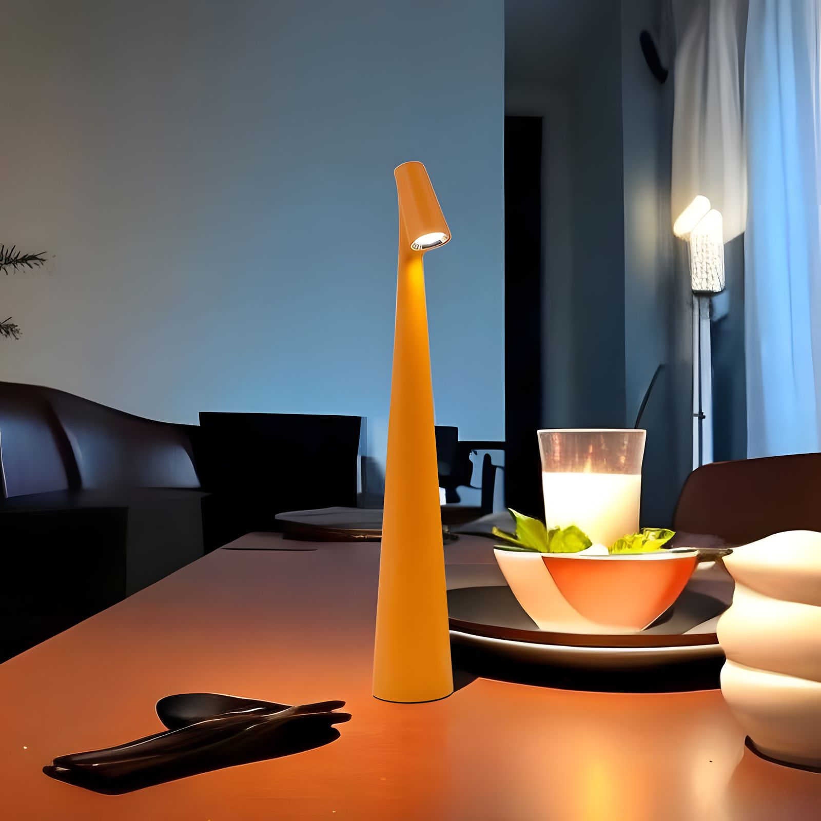 Orange table lamp on a dining table with a candle and bowl in a room setting.