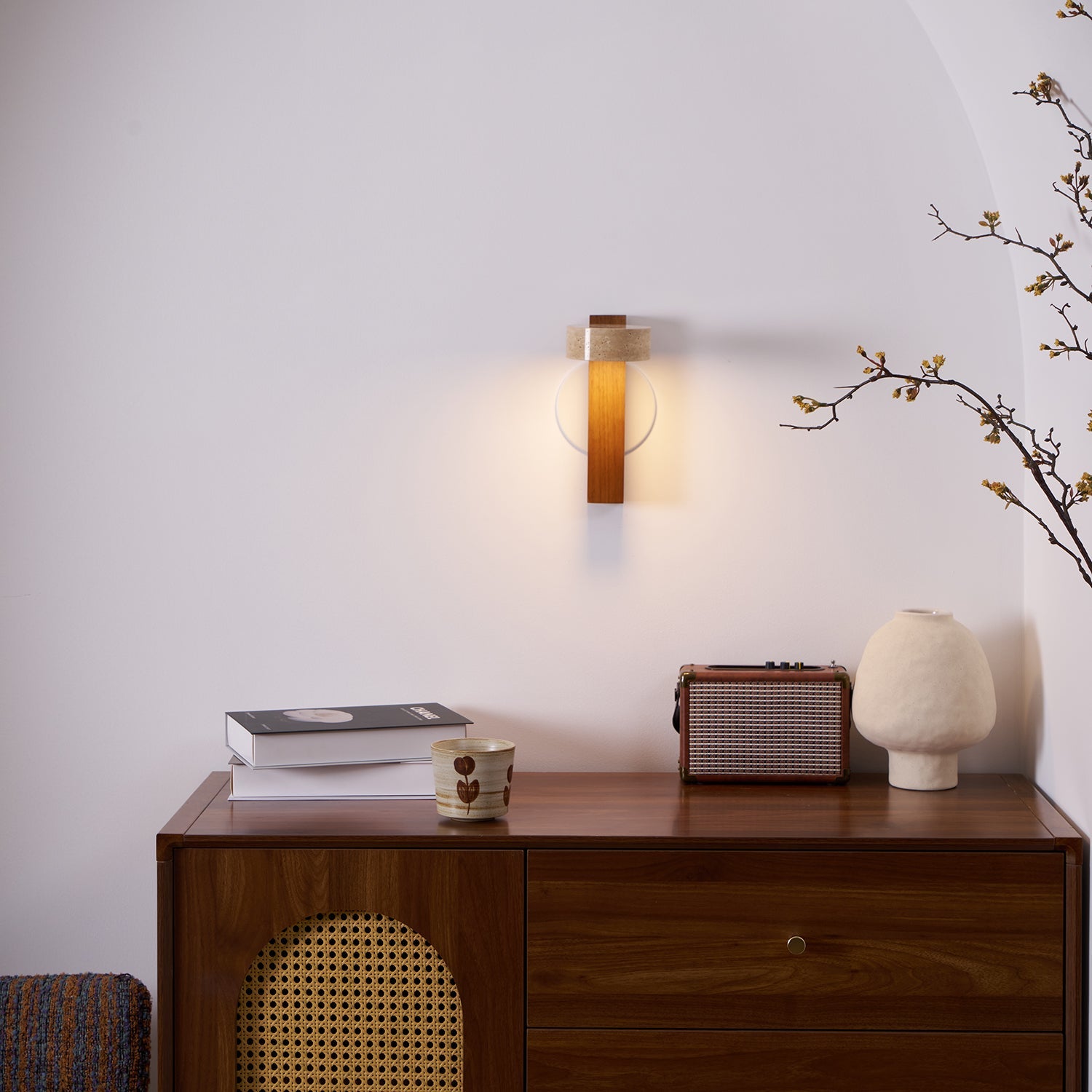 Modern wall sconce lighting fixture on a white wall with decorative items on a wooden console table.