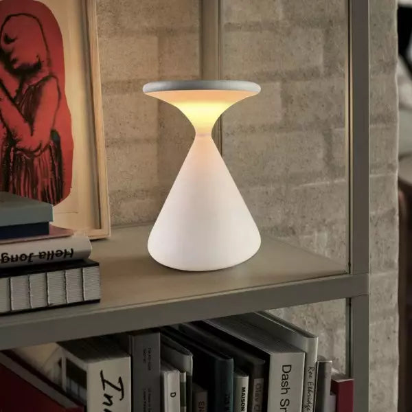 White lamp on a shelf with books and a framed picture in the background