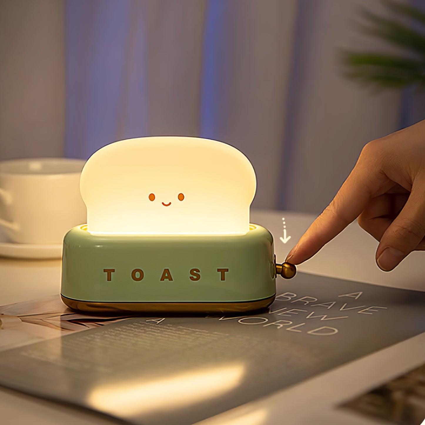 Light-up toaster-shaped night light with a smiling face, being pressed by a hand on a table.