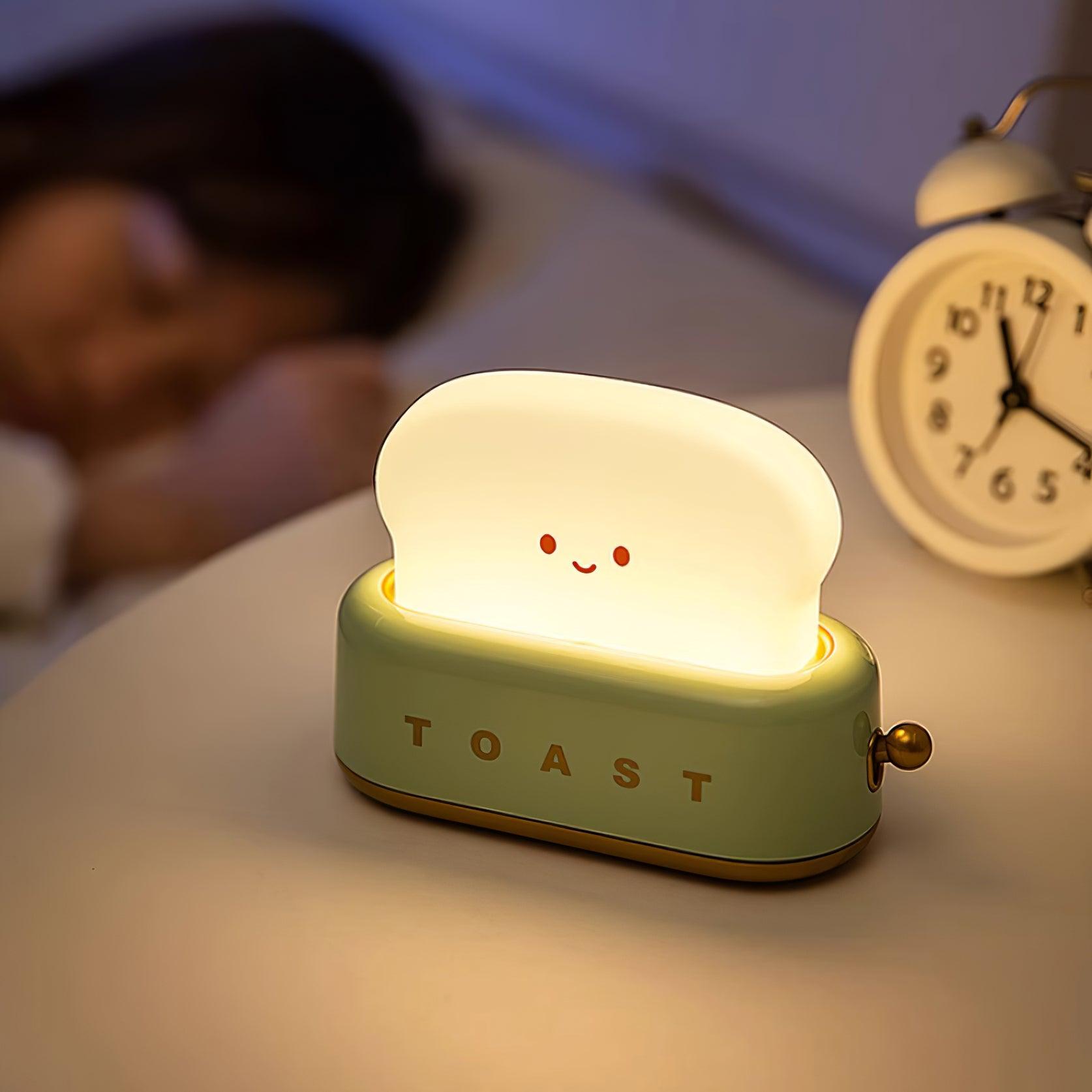 Light-up toaster-shaped night light on a bedside table with a person and alarm clock in the background.