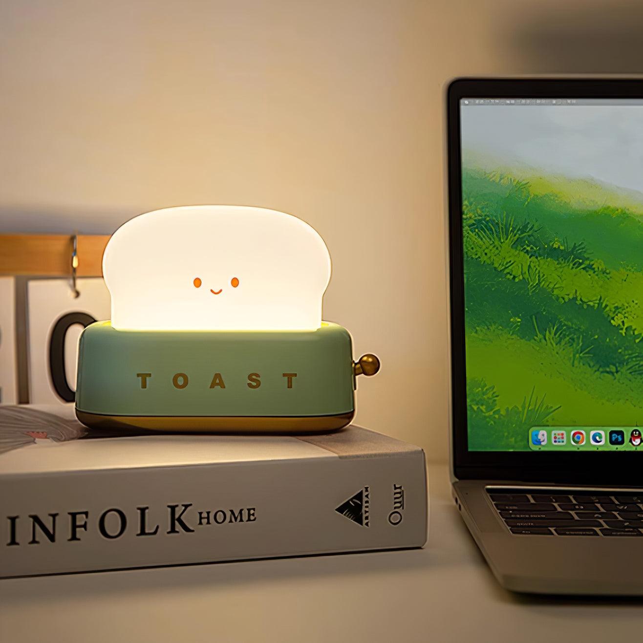 Light-hearted night light labeled 'TOAST' on a book next to a laptop.