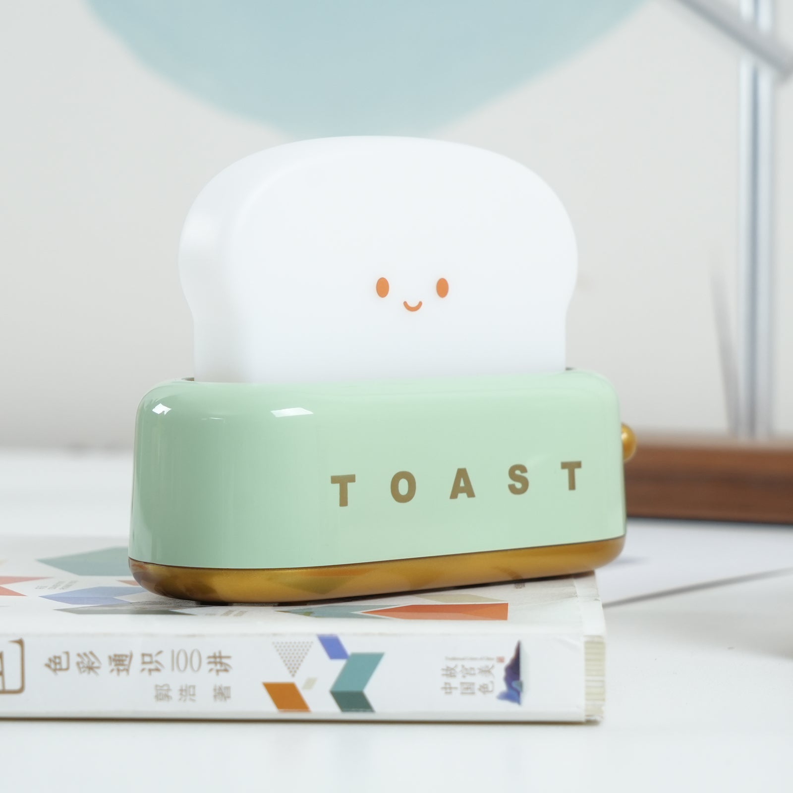 Small toaster with a smiling face on top, sitting on books with a light background