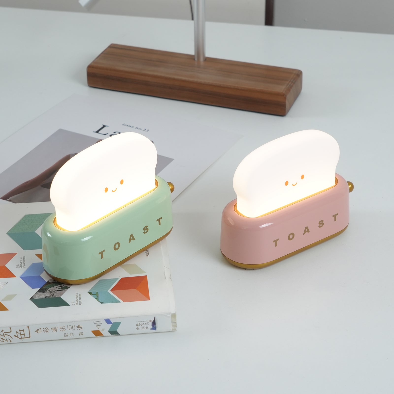 Two cute toast-shaped night lights, one green and one pink, on a table with books.