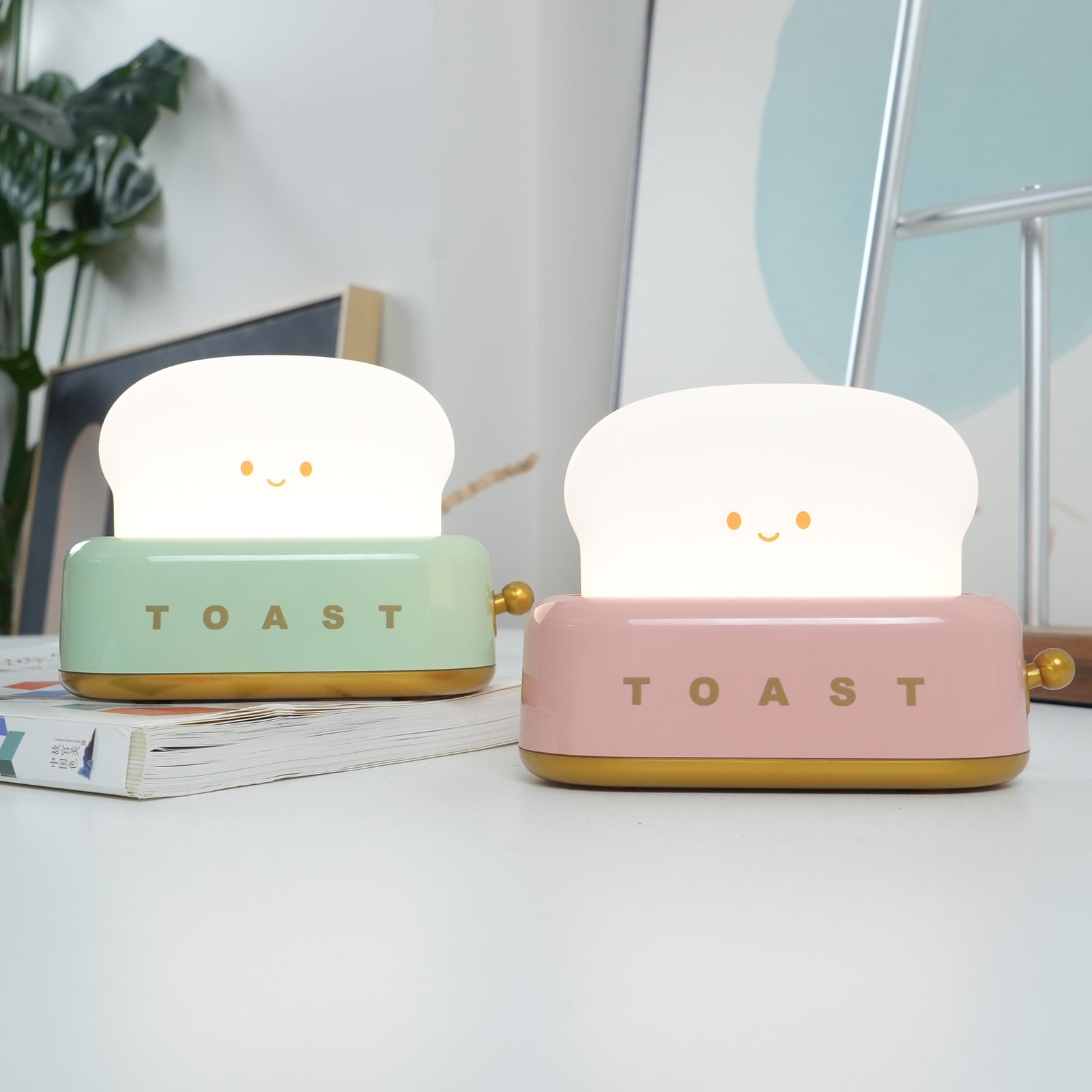 Two cute toaster-shaped night lights, one green and one pink, on a surface with a light background.