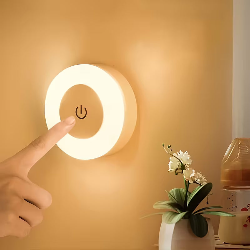 Wall-mounted night light being turned on with a hand, next to a potted plant and baby monitor.