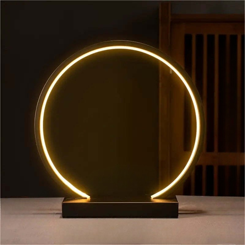 Modern table lamp with circular design and glowing light on a dark background