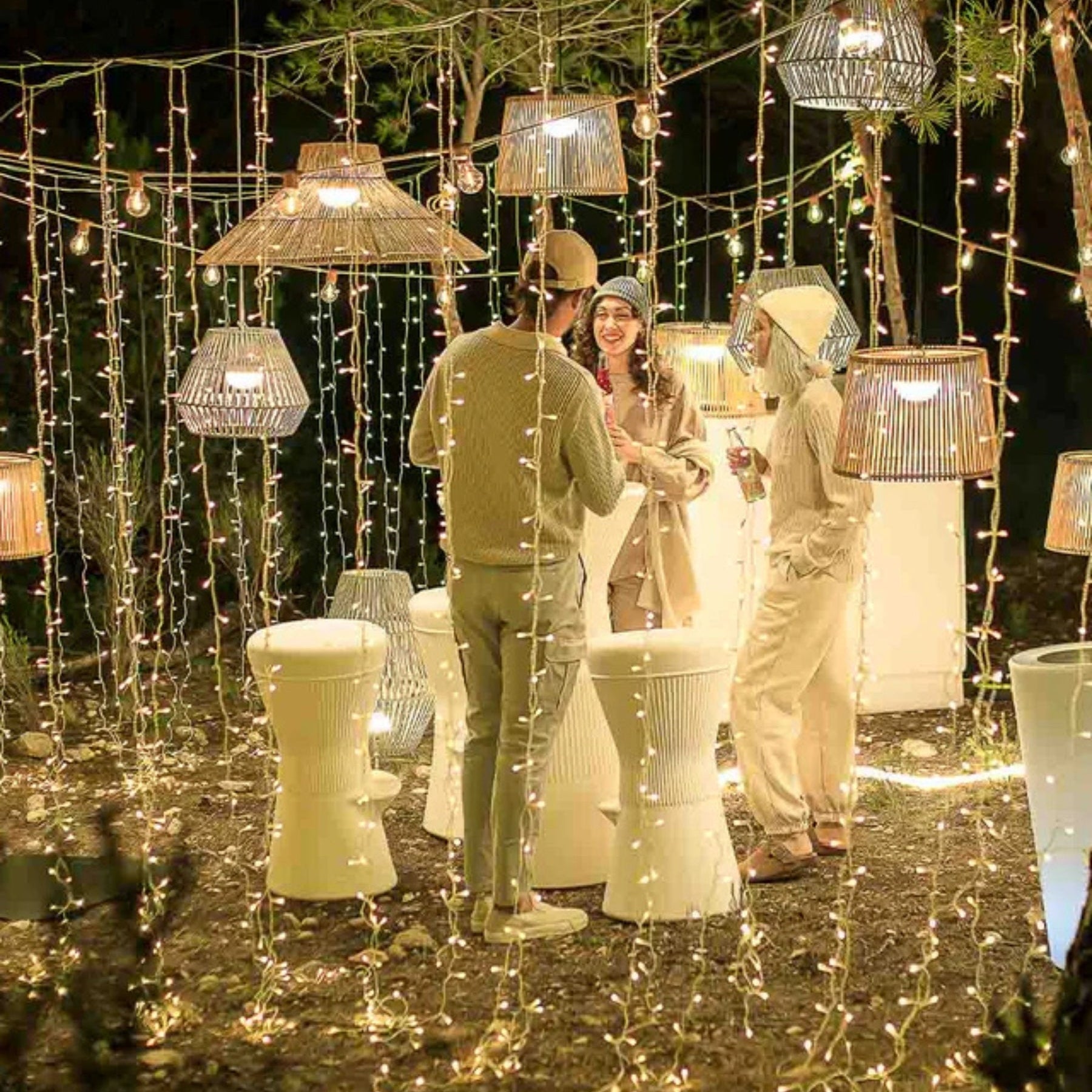 People socializing under string lights and decorative lamps in an outdoor setting.