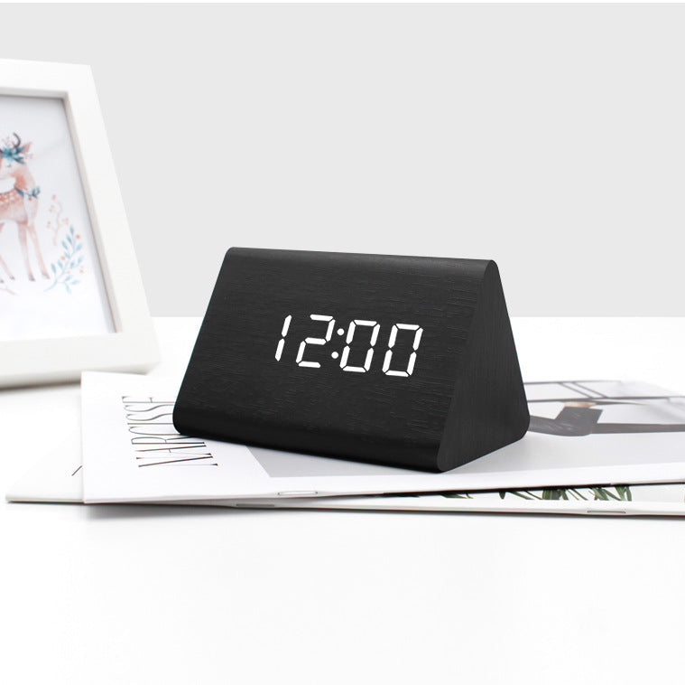 Black digital clock displaying the time on a white surface with a photo frame in the background