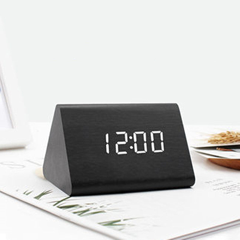 Black triangular digital clock displaying the time on a white surface with a magazine.