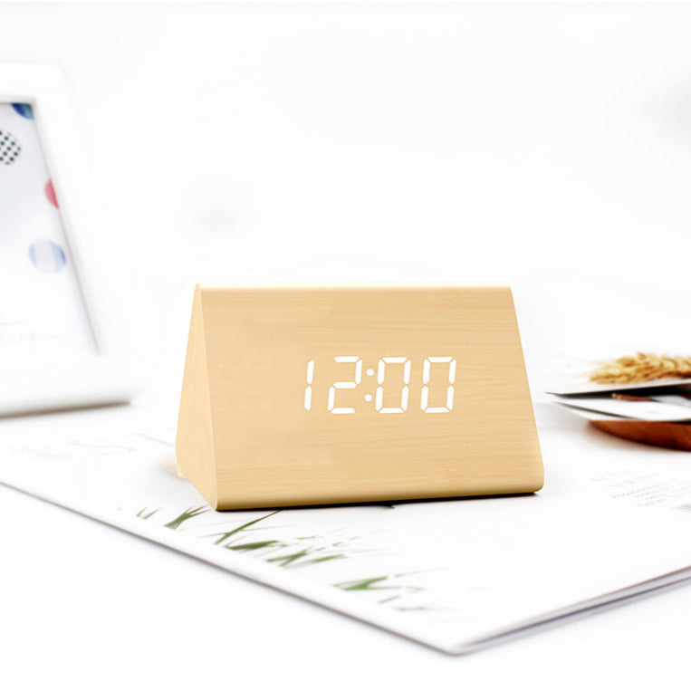 Beige triangular digital clock displaying the time on a white surface with a magazine.