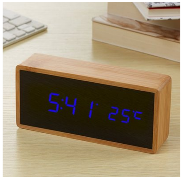 Digital clock with wooden frame displaying time and temperature on a desk.