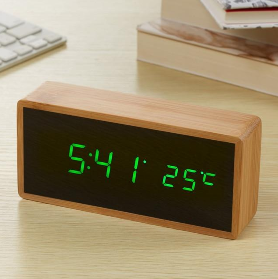 Digital clock with wooden frame displaying time, temperature, and date on a desk.