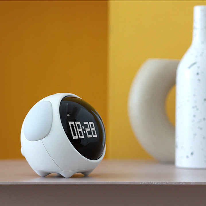 White digital clock on a wooden surface with a yellow wall in the background